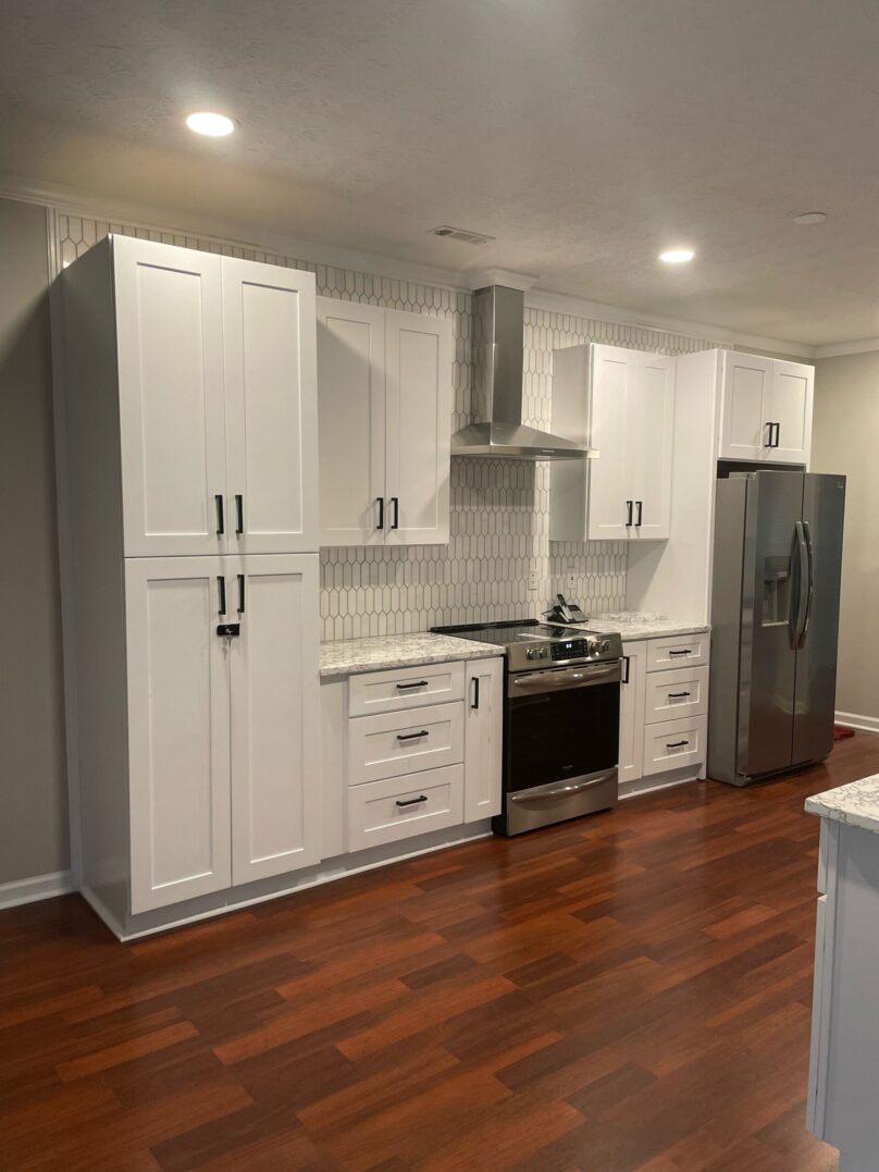 Modern white kitchen with stainless steel appliances and wooden floor.