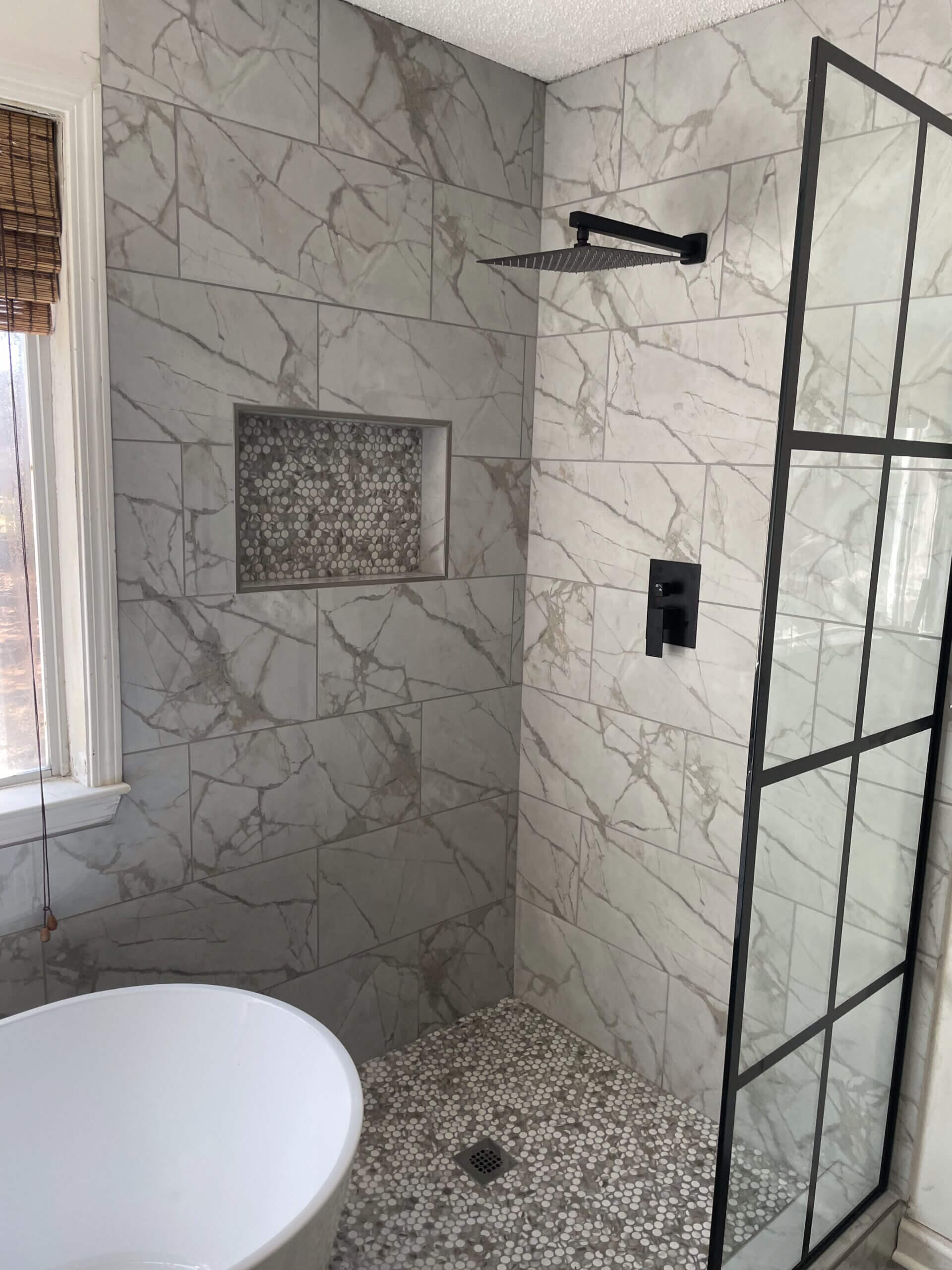 Modern marble bathroom shower with built-in niche and black fixtures.
